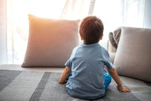 Rear view of child sitting on a bed looking out a window with pillows in front of it; when custody agreements no longer work the court can amend the terms